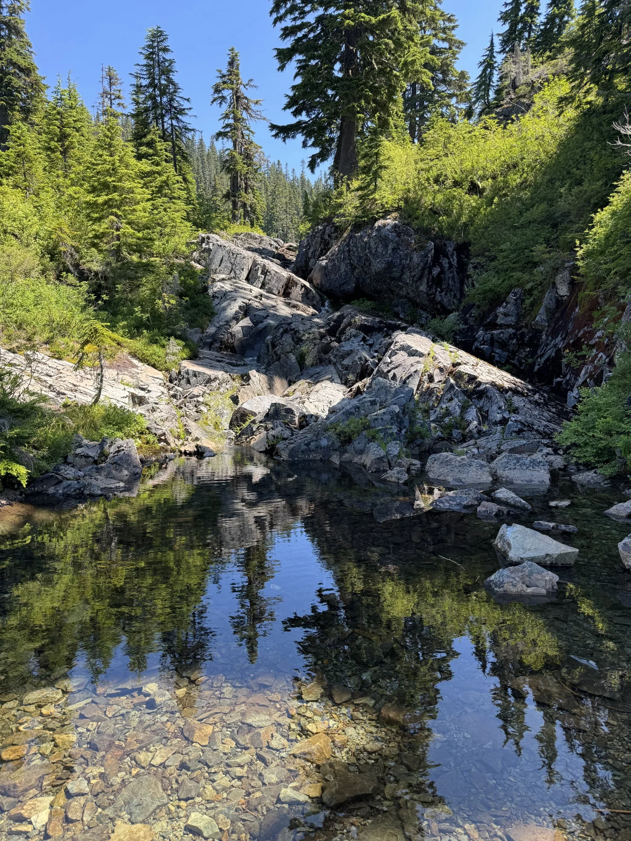 Angled rock with a stream running through it, dropping off to a small reflective pond.