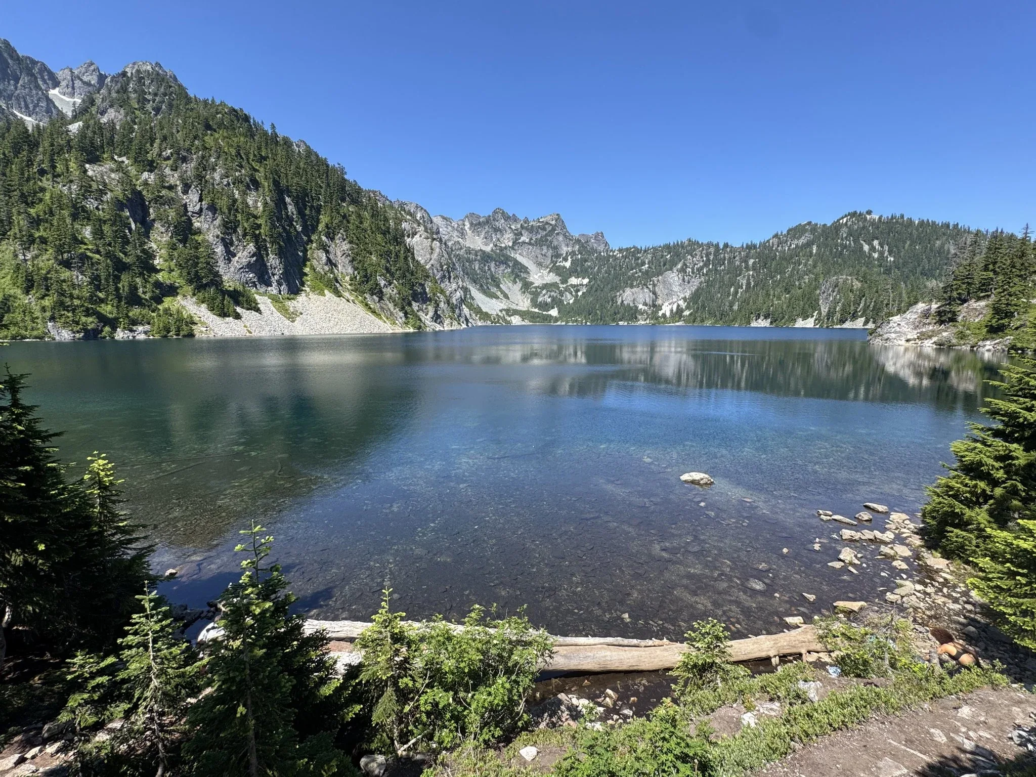 The shore of Snow Lake with shallow water showing the rocks and dirt below the water. A mountanous ridge is around the back end of the lake.